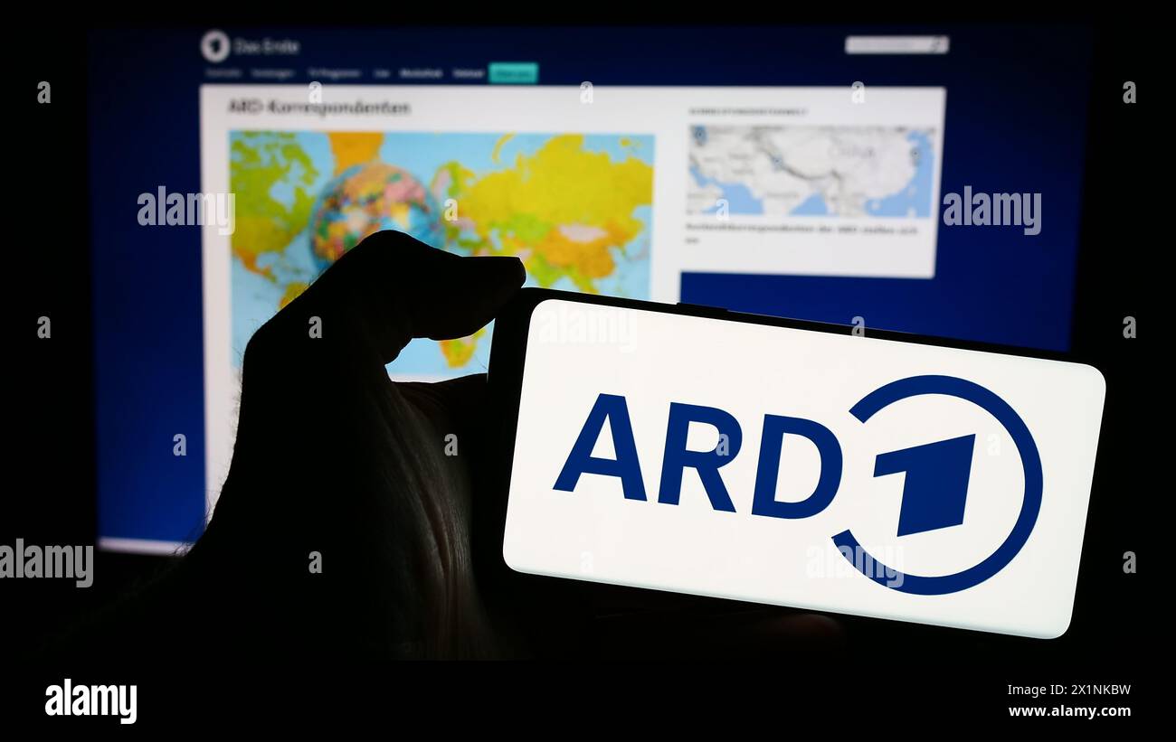 Person holding mobile phone with logo of German public-service broadcasting organisation ARD in front of web page. Focus on phone display. Stock Photo