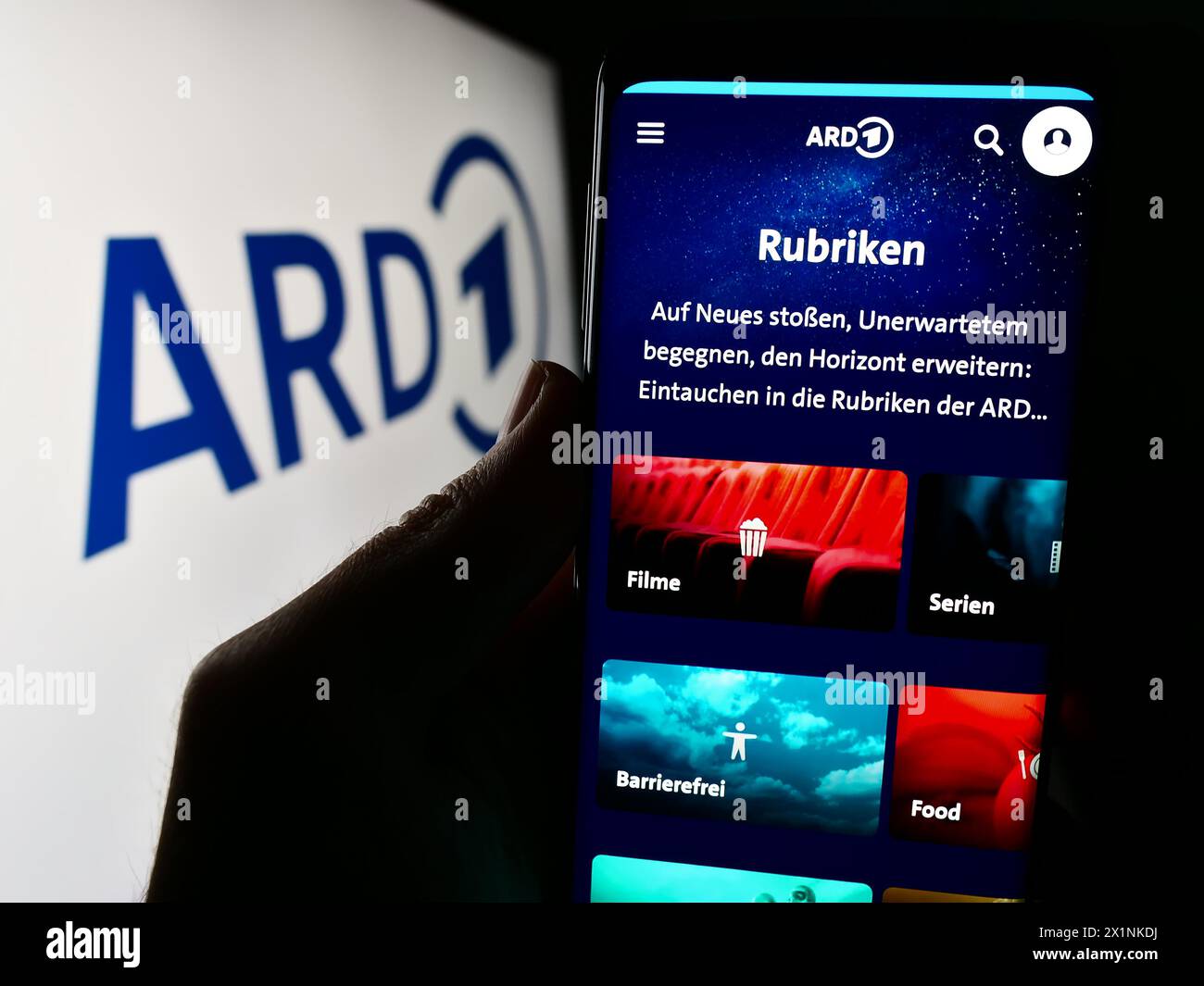 Person holding cellphone with webpage of German public-service broadcasting organisation ARD in front of logo. Focus on center of phone display. Stock Photo