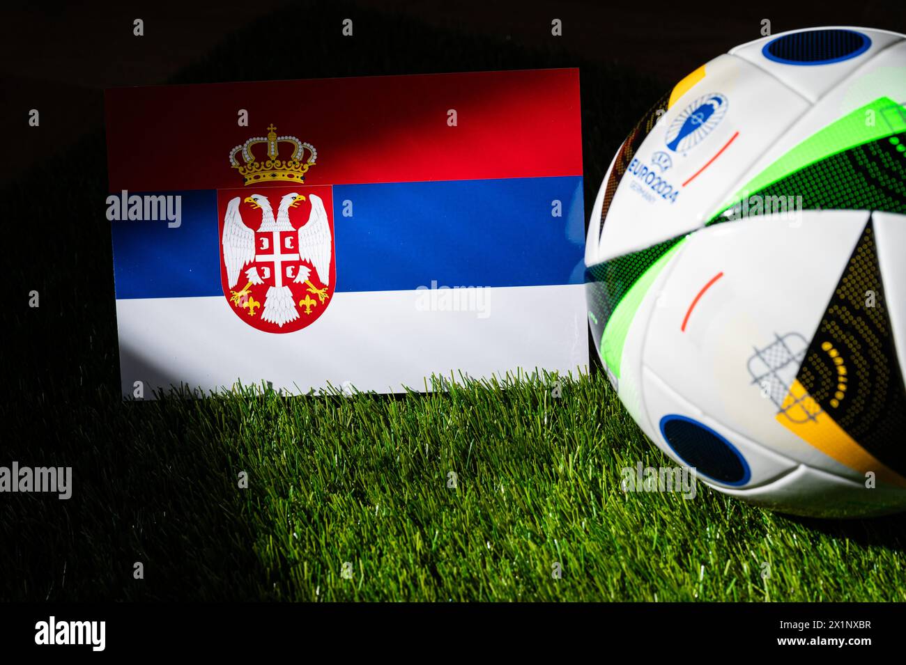 LEIPZIG, GERMANY, APRIL 17, 2024: Serbia national flag and official soccer ball of Euro 2024 football tournament in Germany placed on green grass. Bla Stock Photo