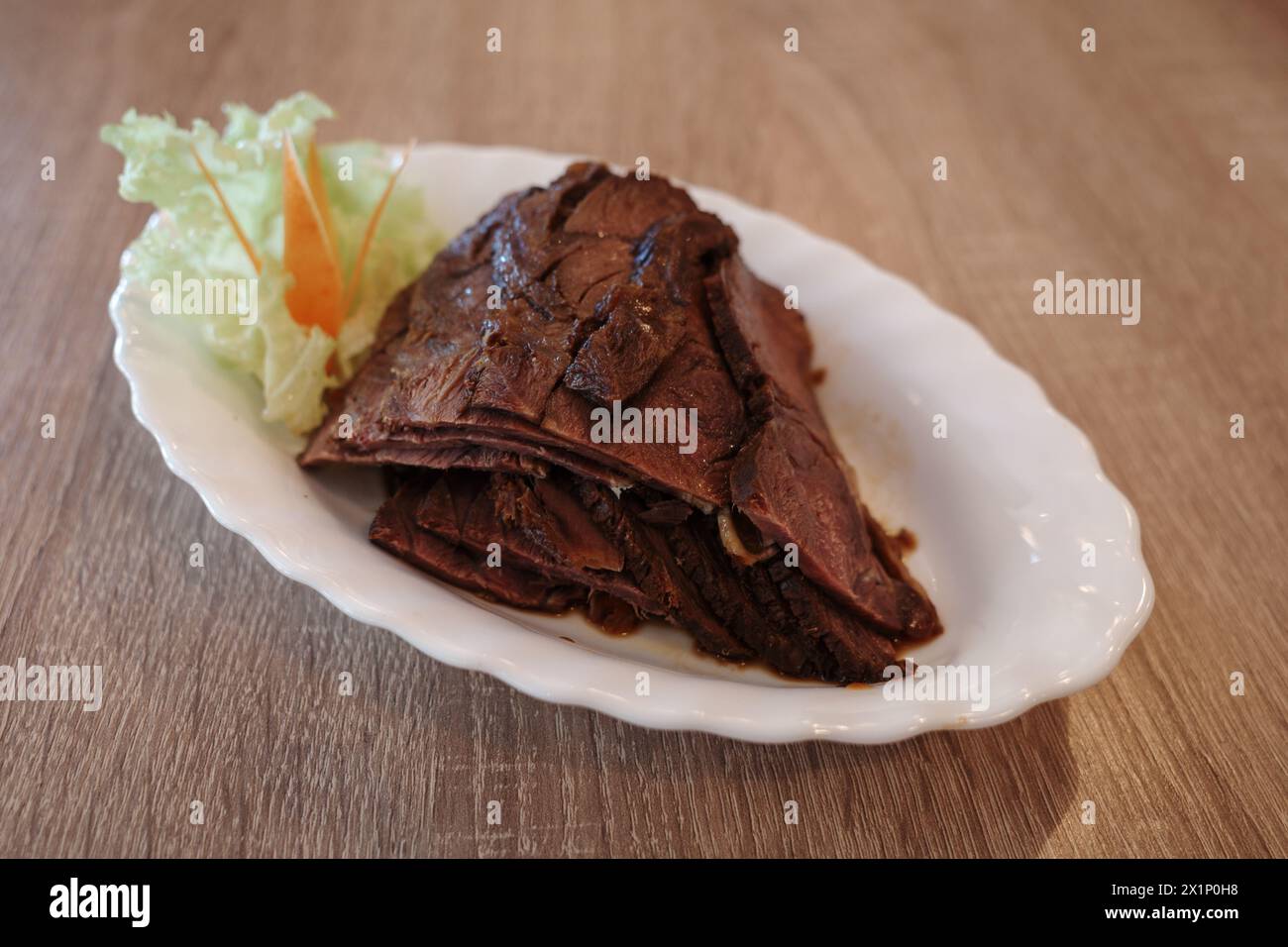 A delectable serving of thinly sliced roast beef, arranged neatly on a white oval plate, accompanied by a simple garnish of lettuce and carrot sticks. Stock Photo