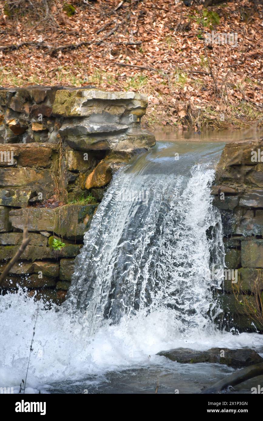 Water pours over the stone wall of the Historic Bush Mill Dam spillway ...