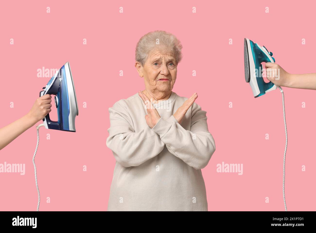 Displeased senior woman showing stop gesture and hands with irons on pink background Stock Photo