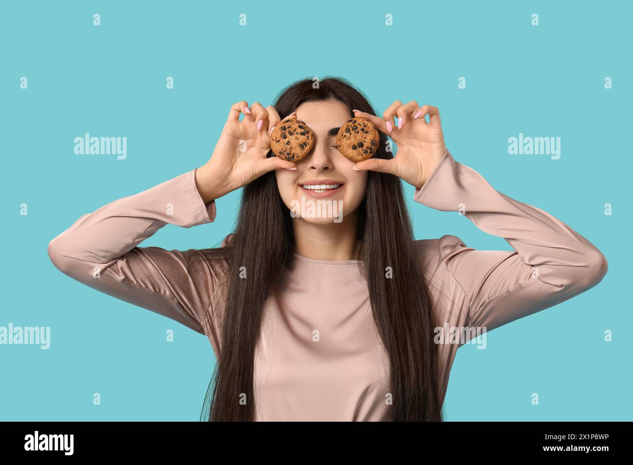 Beautiful young happy woman holding tasty cookies with chocolate chips on blue background Stock Photo