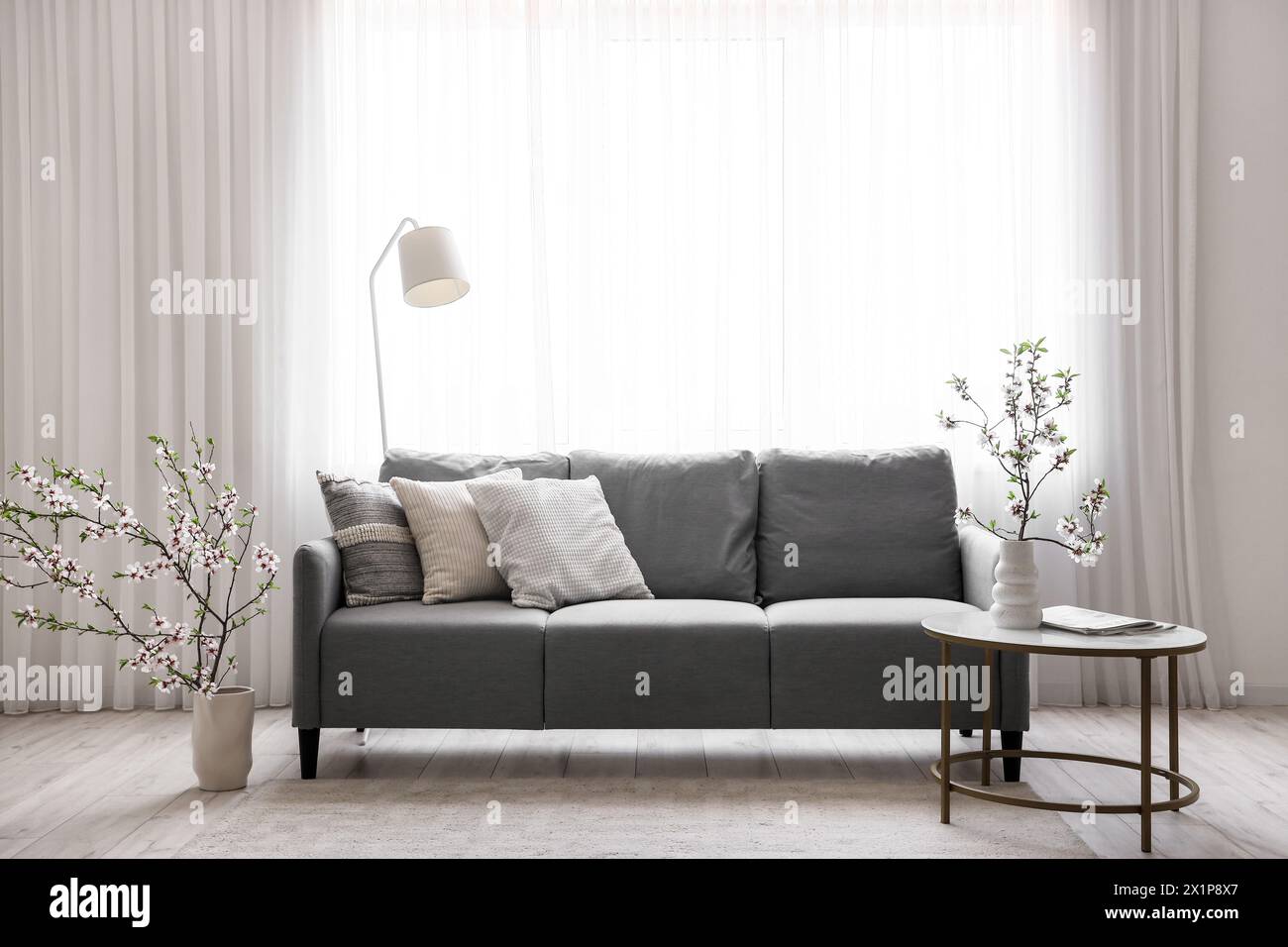 Grey sofa and vase with blooming branches on coffee table in interior of light living room Stock Photo