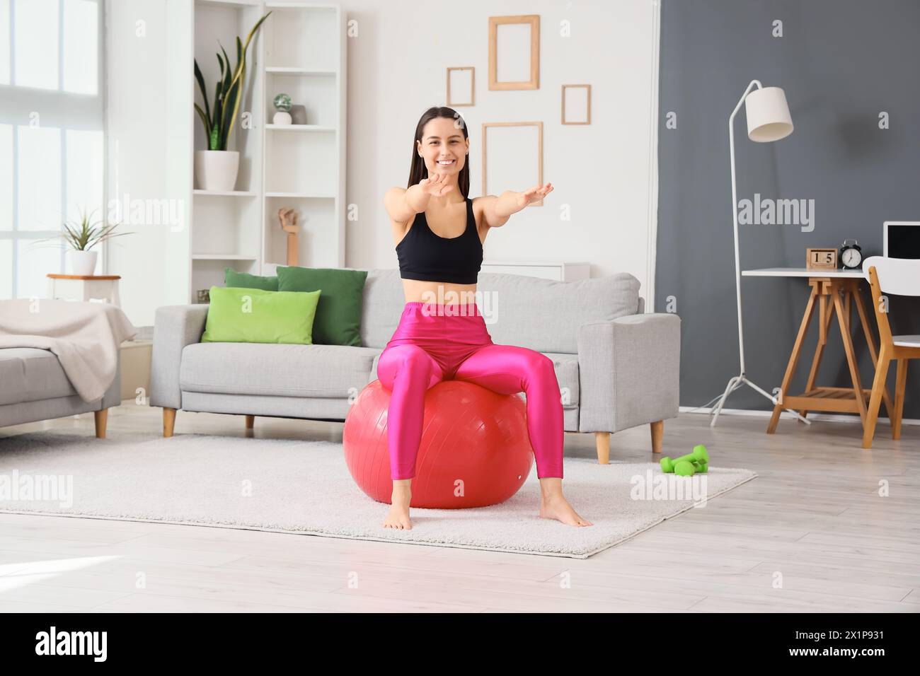 Sporty young woman exercising on fitness ball at home Stock Photo