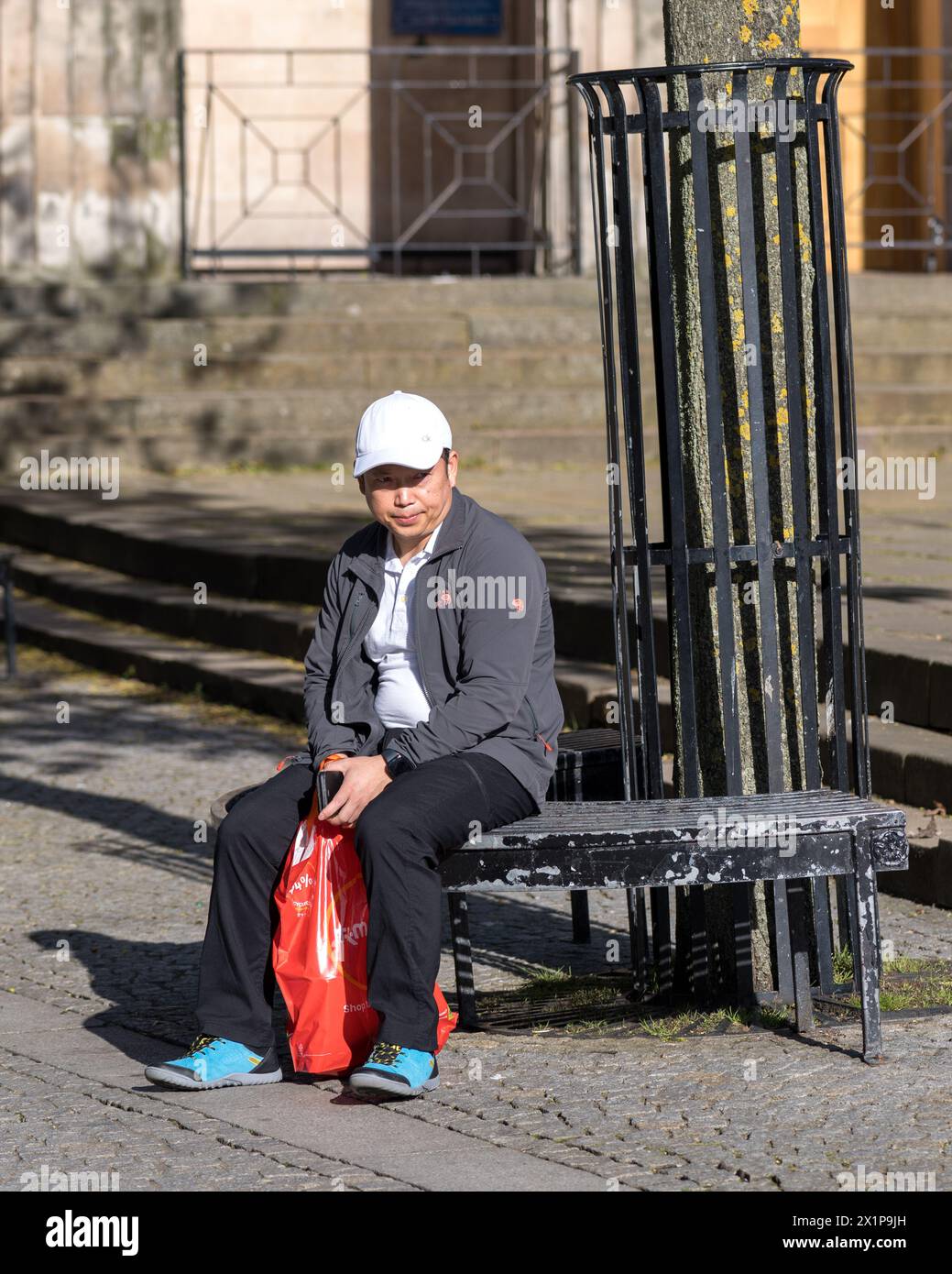 17 April 2024. Elgin,Moray,Scotland. This is an oriental man on holiday sitting enjoying the sunshine on Elgin High Street pedestrian area. Stock Photo