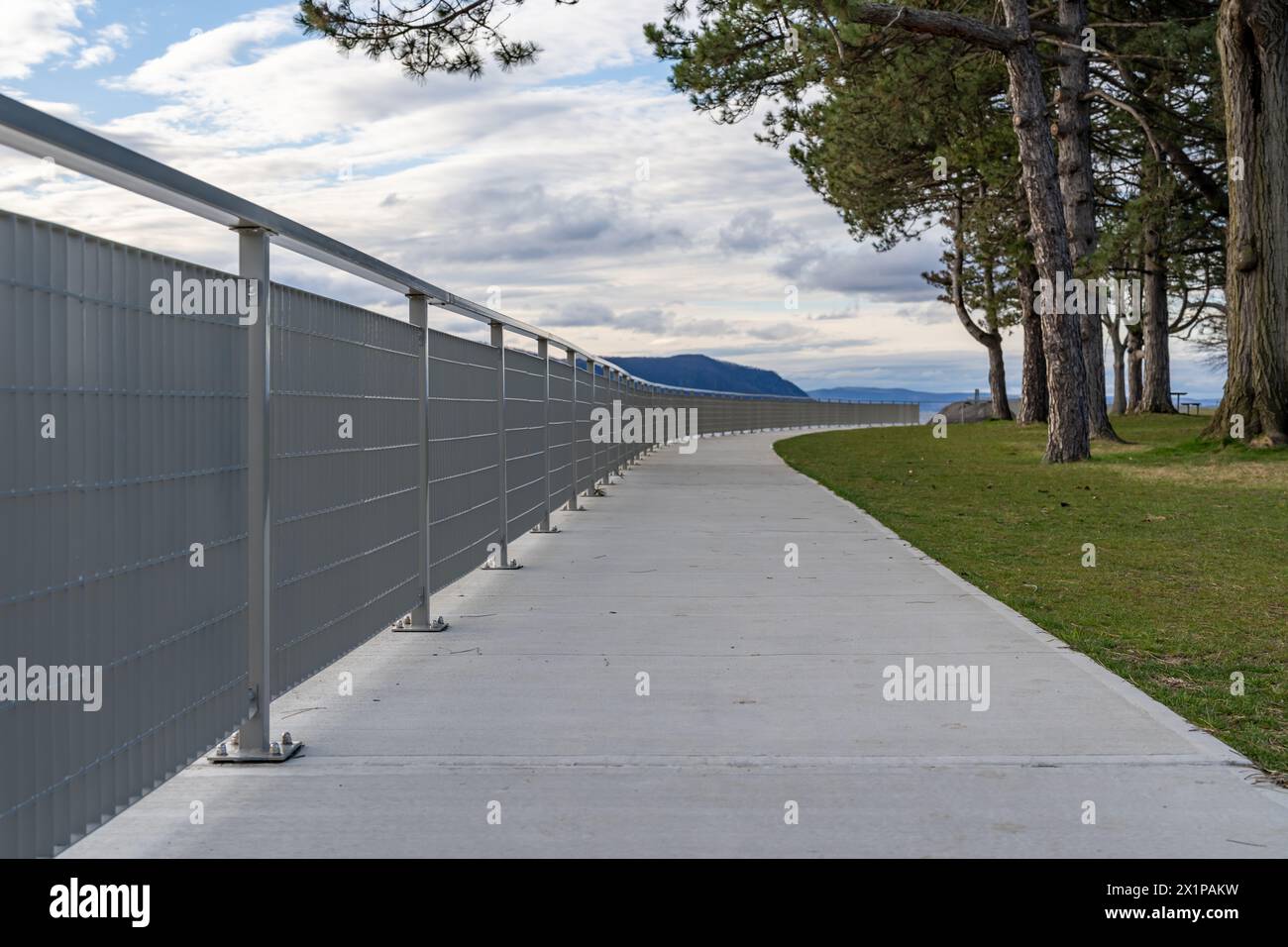 Example of a stainless steel railing along a concrete sidewalk, at the top of retaining wall. Stock Photo