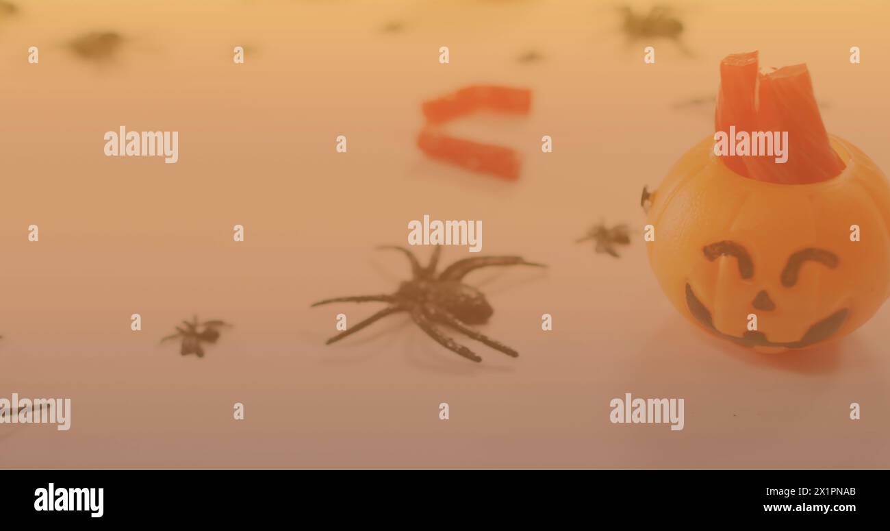 A small pumpkin decoration sitting among plastic spiders on surface Stock Photo