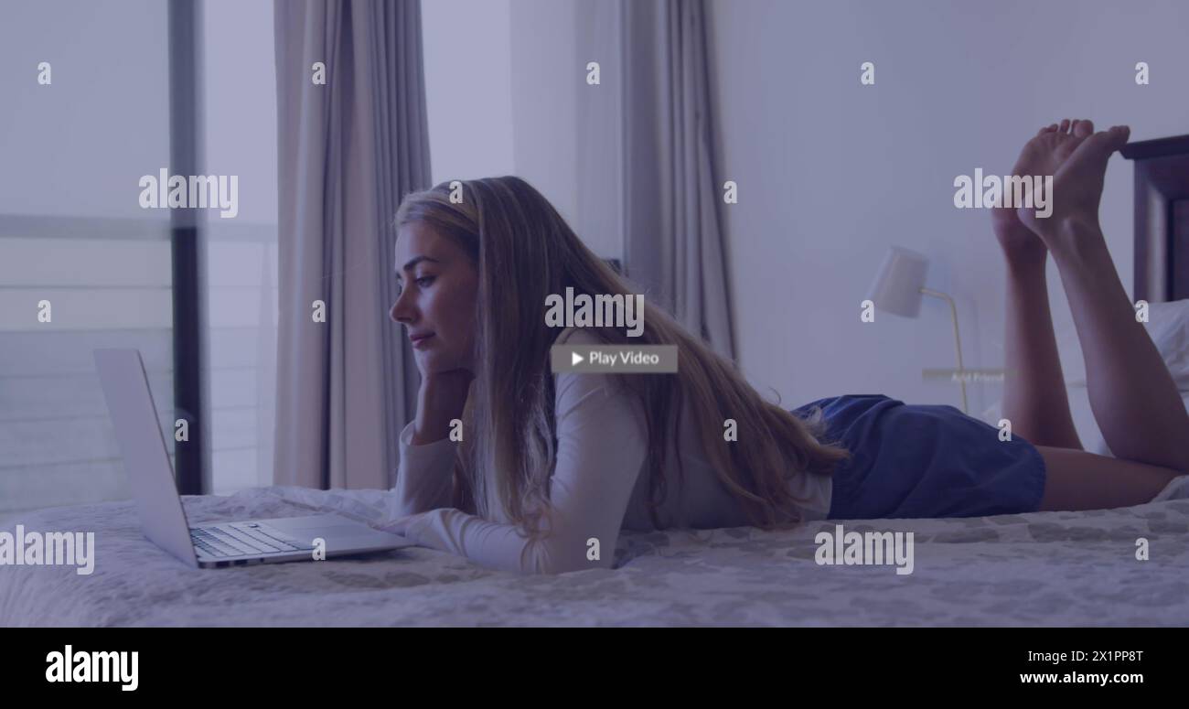 Caucasian young woman lying on bed, looking at laptop Stock Photo