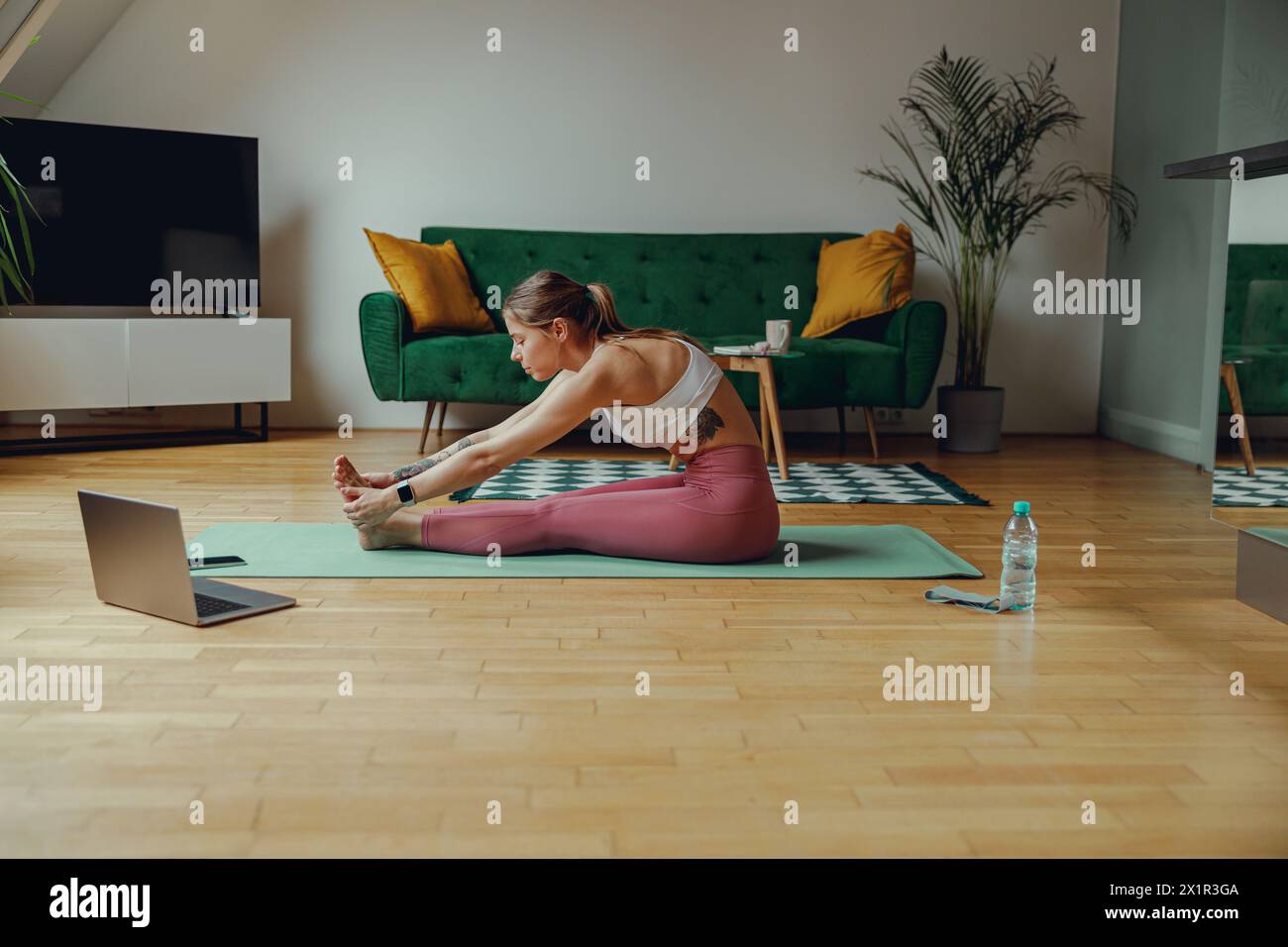 Sporty woman doing stretching exercises on a yoga mat in a living room Stock Photo