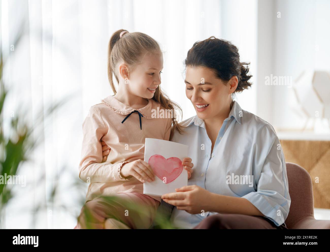 Happy mother's day. Child daughter is congratulating mom and giving her postcard. Mum and girl smiling and hugging. Family holiday and togetherness. Stock Photo