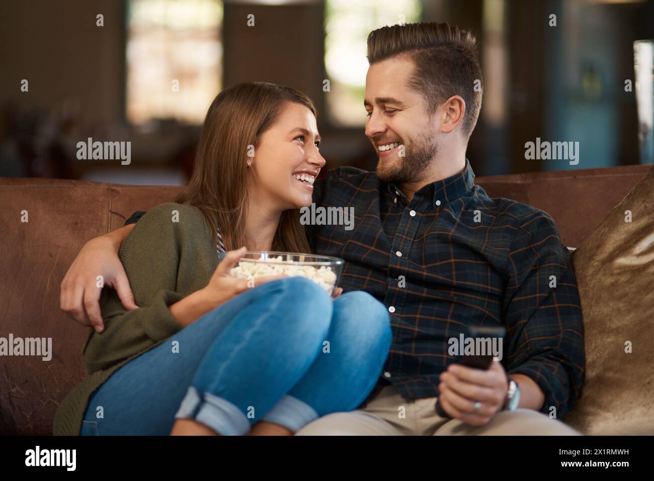 Couple, hug and popcorn or remote for tv on couch, relax and bonding with movie snack in home. Happy people, embrace and love for series or laugh for Stock Photo