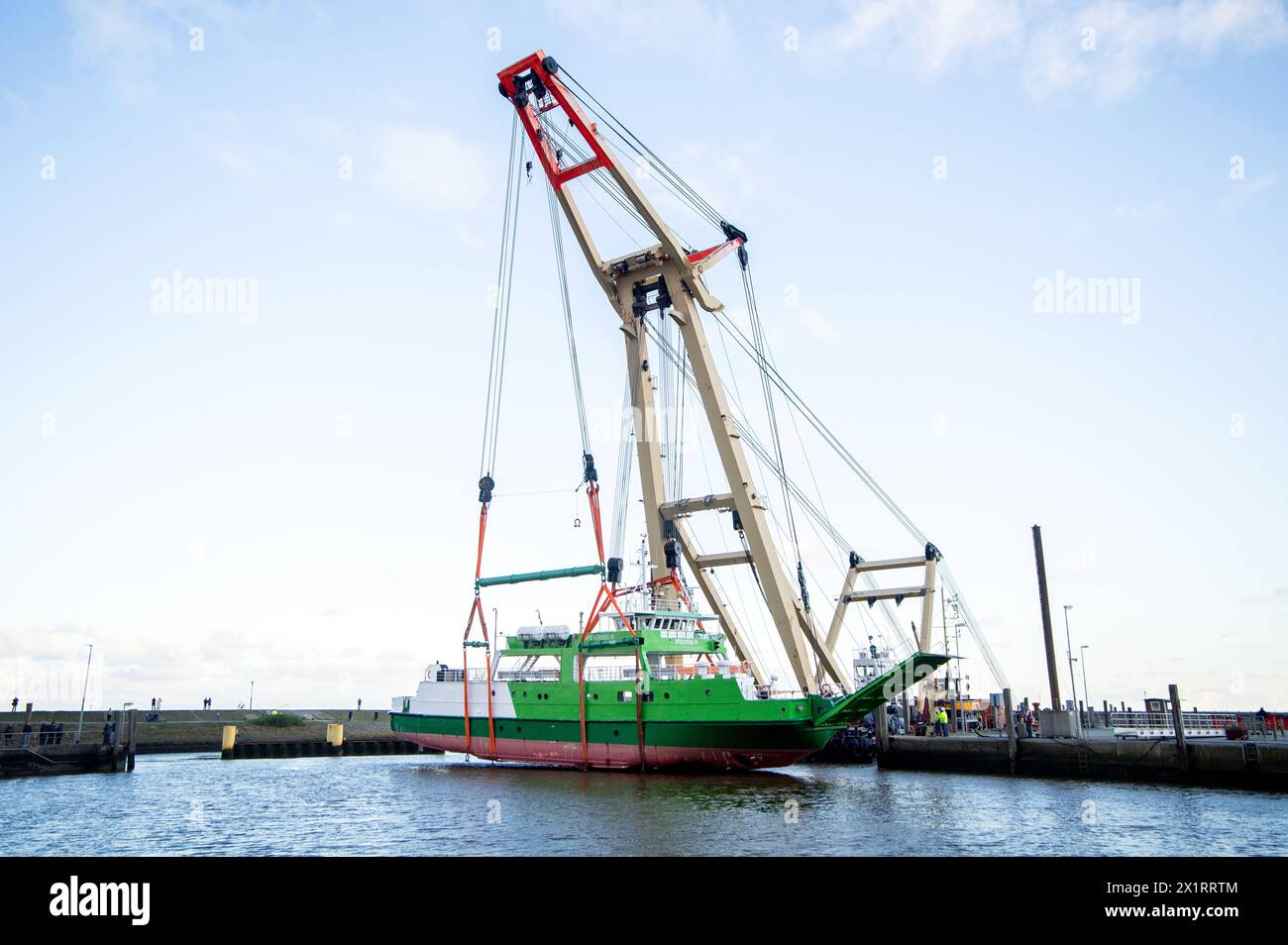 Neuharlingersiel, Germany. 18th Apr, 2024. The floating crane 'Enak' lifts the ferry 'Spiekeroog IV' back into the harbor basin. The 300-ton ship, which is used for ferry services to the East Frisian island of Spiekeroog, had drifted away from its berth during the storm 'Zoltan' in December 2023 and onto a parking area in the harbour. Credit: Hauke-Christian Dittrich/dpa/Alamy Live News Stock Photo