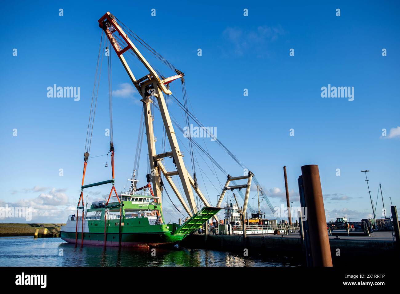 Neuharlingersiel, Germany. 18th Apr, 2024. The floating crane 'Enak' lifts the ferry 'Spiekeroog IV' back into the harbor basin. The 300-ton ship, which is used for ferry services to the East Frisian island of Spiekeroog, had drifted away from its berth during the storm 'Zoltan' in December 2023 and onto a parking area in the harbour. Credit: Hauke-Christian Dittrich/dpa/Alamy Live News Stock Photo