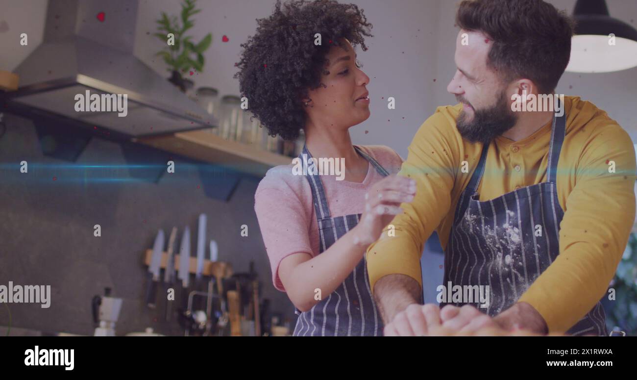 Diverse couple, wearing aprons, standing in kitchen Stock Photo