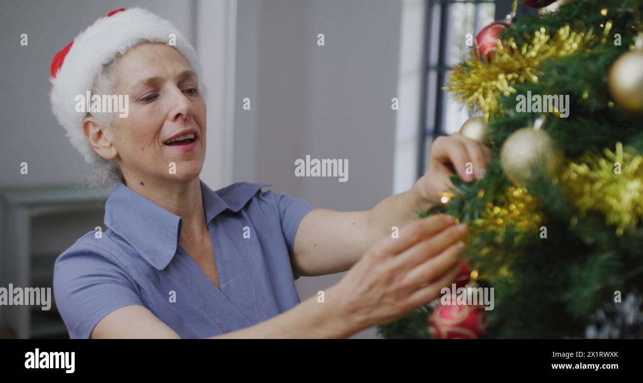 Caucasian senior woman with gray hair is decorating Christmas tree Stock Photo