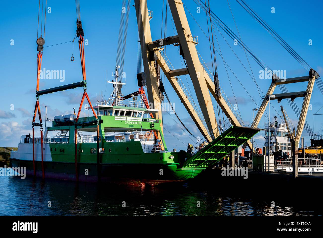 Neuharlingersiel, Germany. 18th Apr, 2024. The floating crane 'Enak' lifts the ferry 'Spiekeroog IV' back into the harbor basin. The 300-ton ship, which is used for ferry services to the East Frisian island of Spiekeroog, had drifted away from its berth during the storm 'Zoltan' in December 2023 and onto a parking area in the harbour. Credit: Hauke-Christian Dittrich/dpa/Alamy Live News Stock Photo