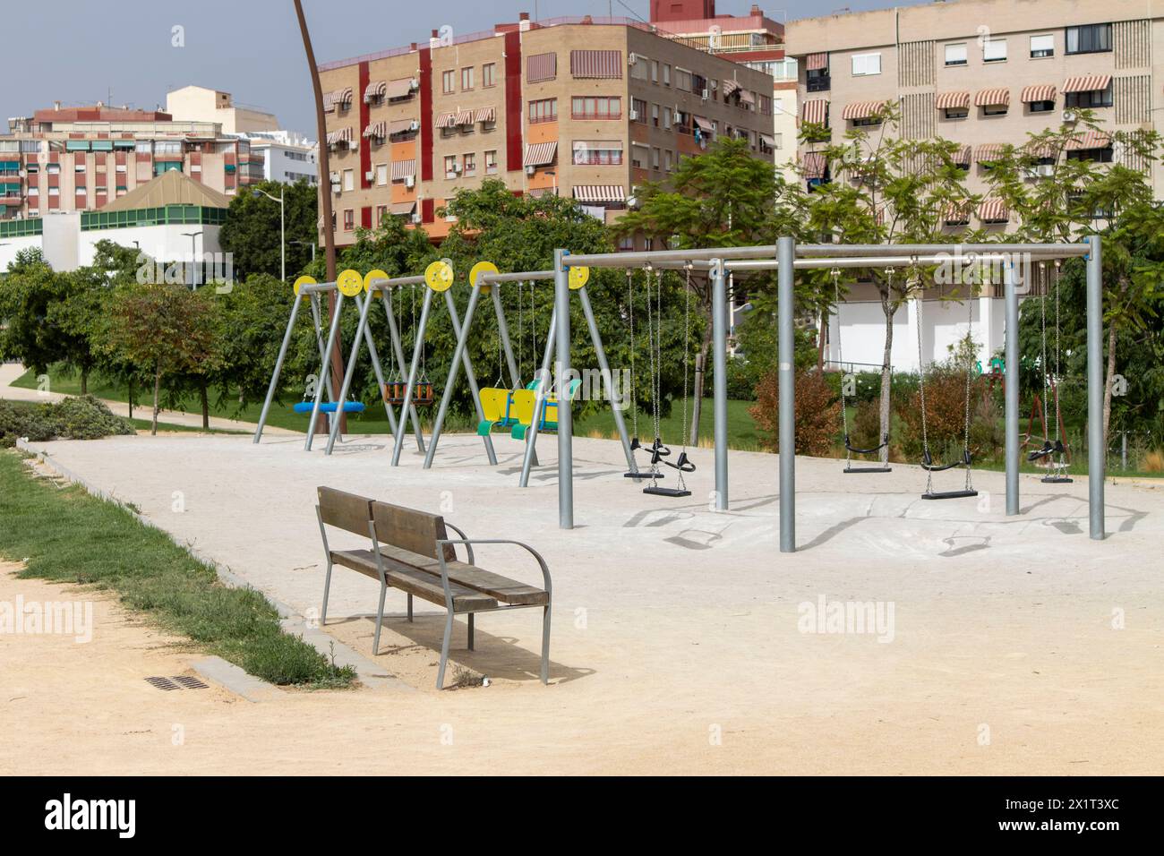 Empty swing set in a peaceful park with city backdrop. Stock Photo