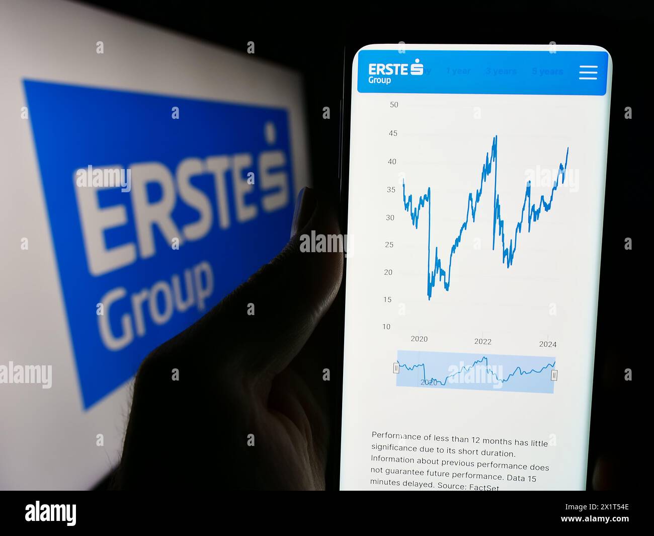 Person holding cellphone with website of Austrian financial services company Erste Group Bank AG with logo. Focus on center of phone display. Stock Photo