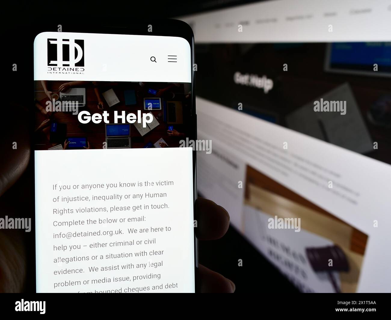 Person holding mobile phone with web page and logo of legal advocacy NGO Detained International. Focus on center of phone display. Stock Photo