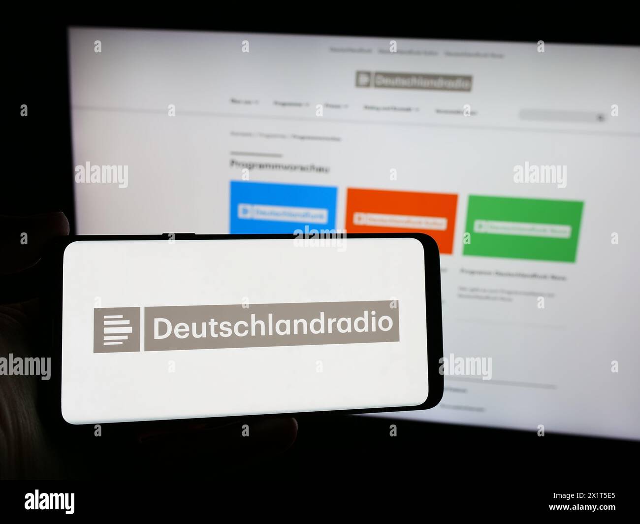 Person holding smartphone with logo of German public radio broadcaster Deutschlandradio in front of website. Focus on phone display. Stock Photo