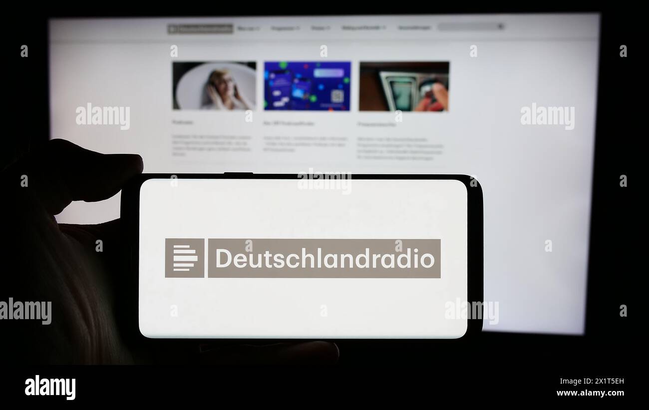 Person holding cellphone with logo of German public radio broadcaster Deutschlandradio in front of webpage. Focus on phone display. Stock Photo