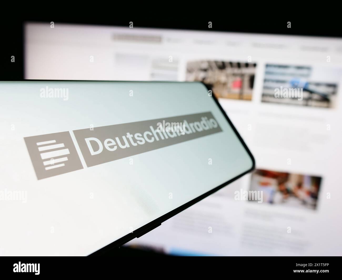 Mobile phone with logo of German public radio broadcaster Deutschlandradio in front of website. Focus on left of phone display. Stock Photo