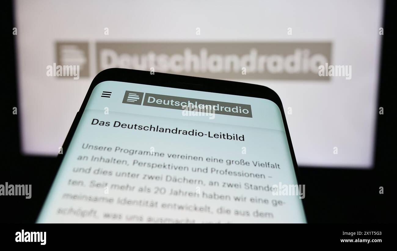 Smartphone with website of German public radio broadcaster Deutschlandradio in front of logo. Focus on top-left of phone display. Stock Photo