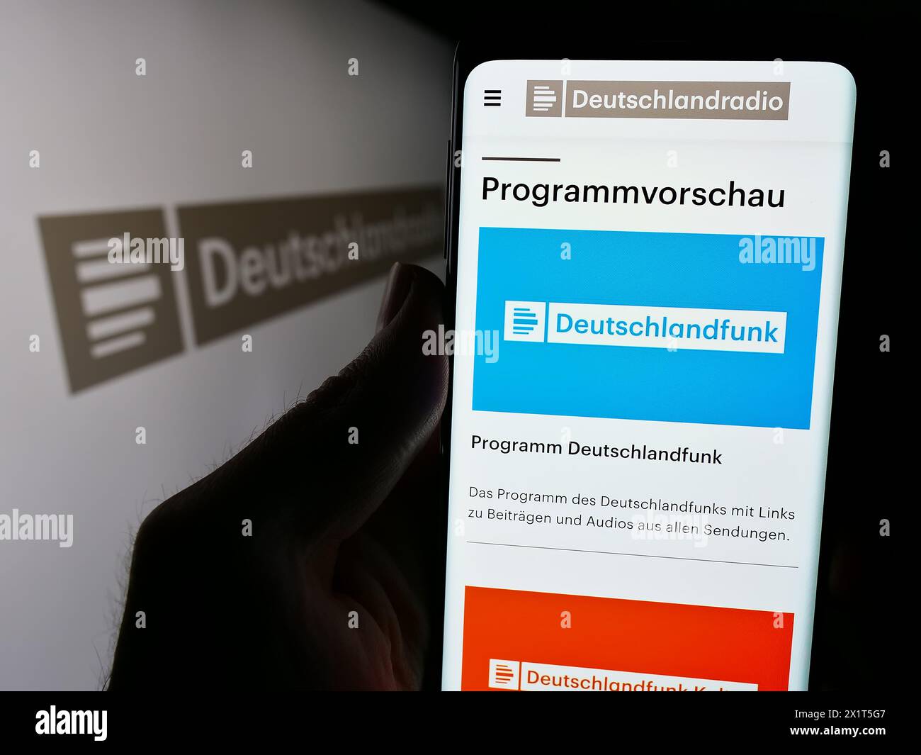 Person holding cellphone with webpage of German public radio broadcaster Deutschlandradio in front of logo. Focus on center of phone display. Stock Photo