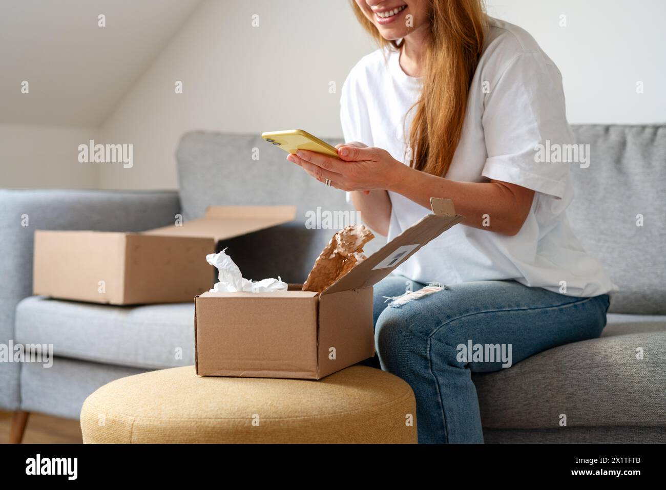 Express delivery. Receiving online purchase. Woman unpacking cardboard and taking pictures of purchases. Stock Photo