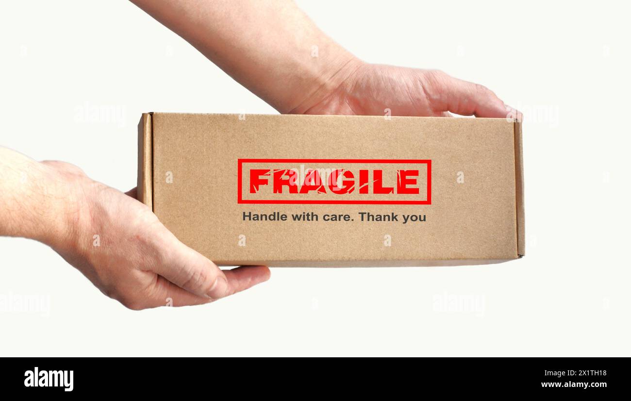 One rectangular cardboard box in hands for fragile items packing on a plain light background. Red warning label, sticker for packaging 'Fragile' Stock Photo