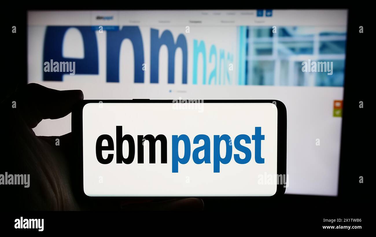 Person holding cellphone with logo of German electric motor company EBM-Papst Gruppe in front of business webpage. Focus on phone display. Stock Photo