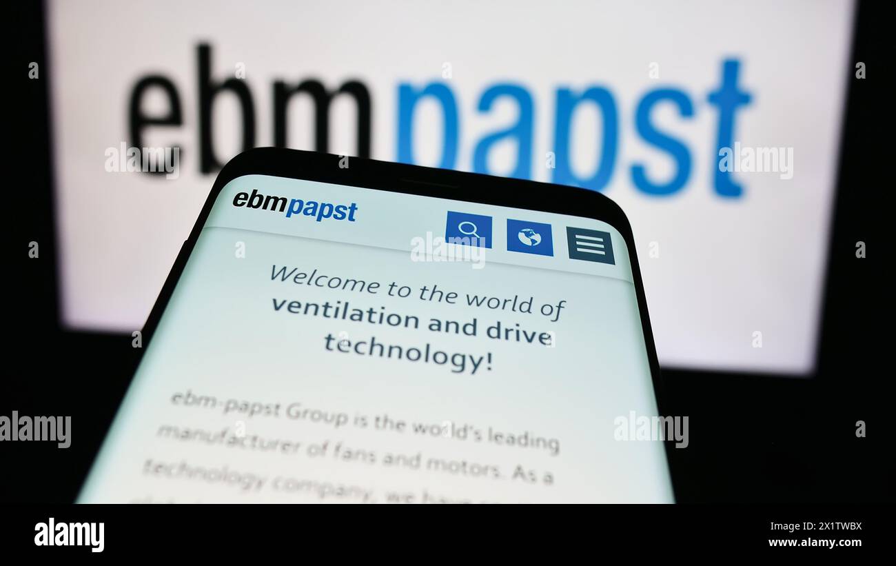 Smartphone with website of German electric motor company EBM-Papst Gruppe in front of business logo. Focus on top-left of phone display. Stock Photo