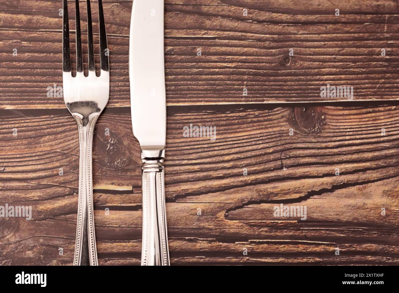 Knife and fork against rustic wood table background with copy space for use as background to menu or similar. Stock Photo
