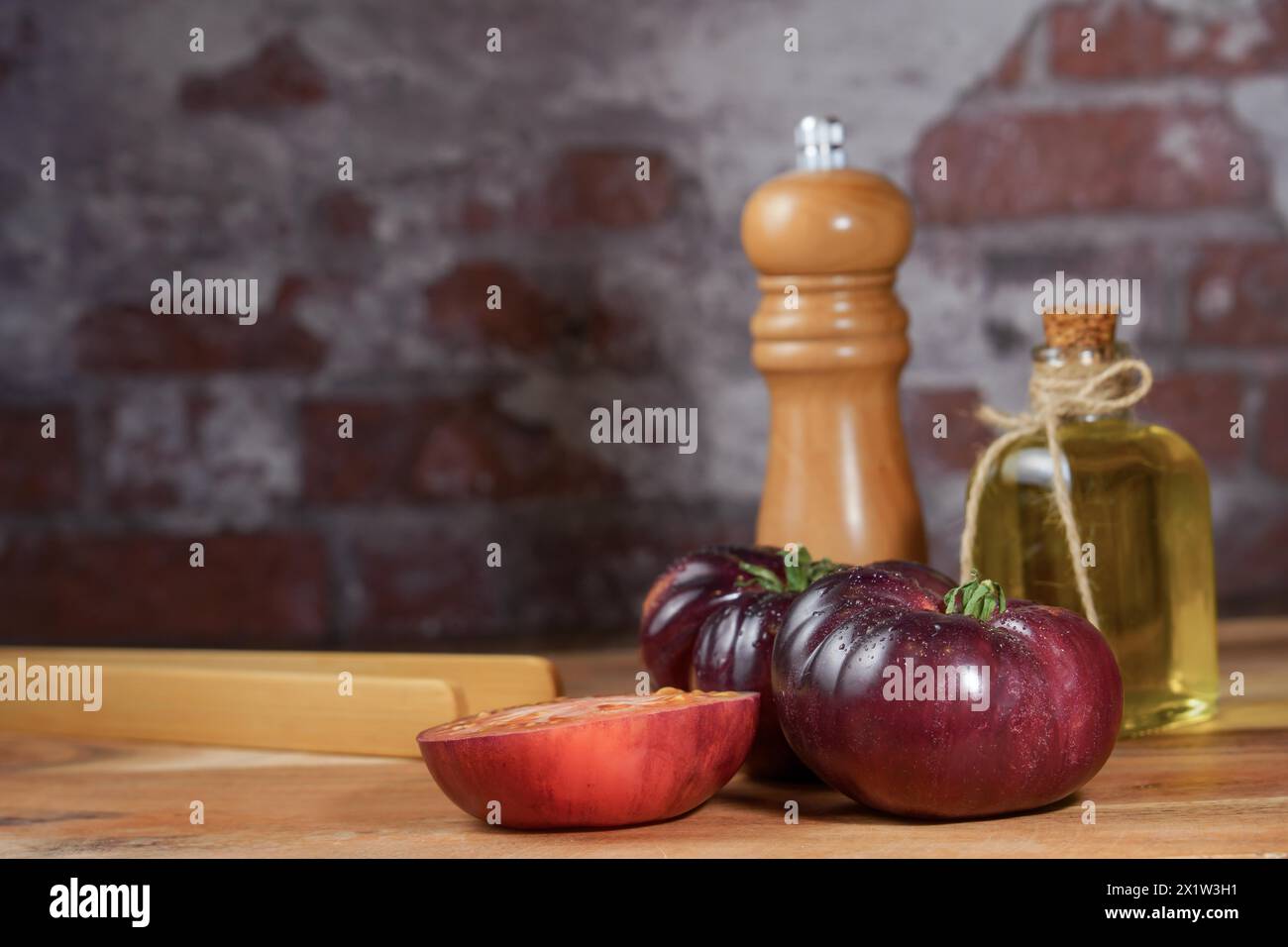 Group of tasty fresh tomatoes of the blue variety together with wooden tongs, a glass bottle of olive oil and a pepper shaker on a wooden table Stock Photo