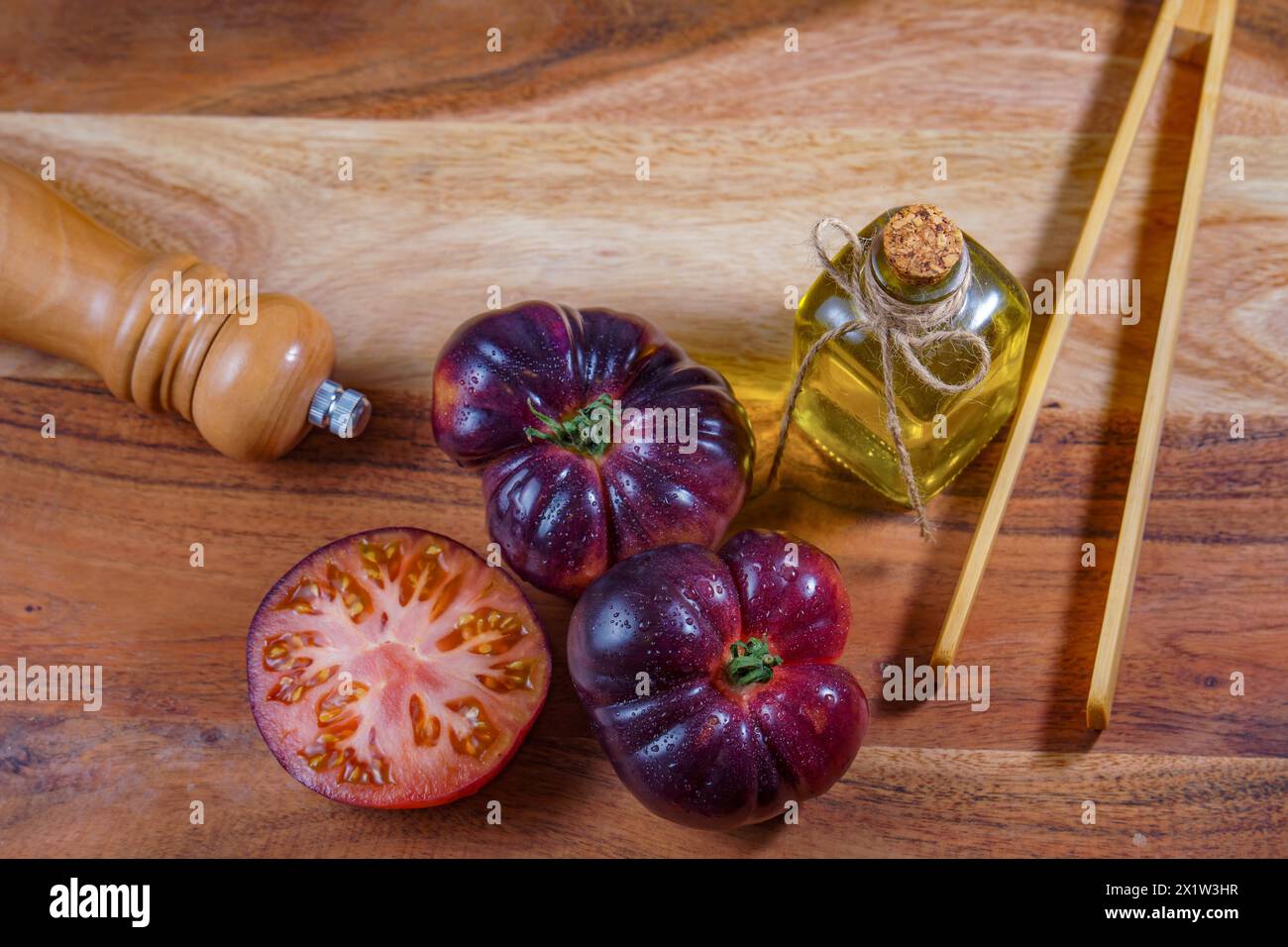 Top view of a group of tasty fresh tomatoes of the blue variety next to some wooden tongs, olive oil and a pepper shaker on a wooden table Stock Photo