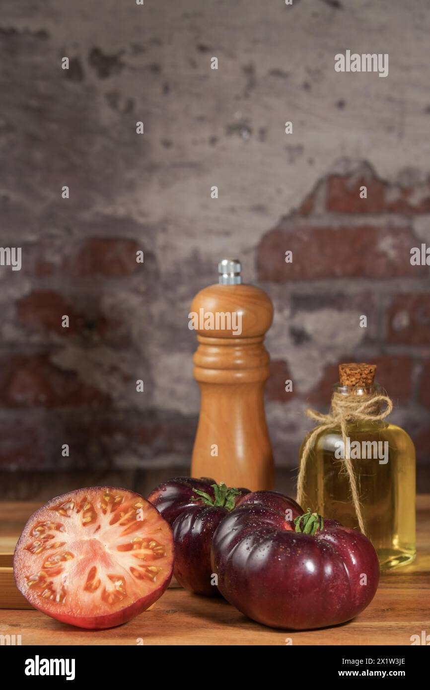 Group of tasty fresh tomatoes of the blue variety together with wooden tongs, a glass bottle of olive oil and a pepper shaker on a wooden table Stock Photo