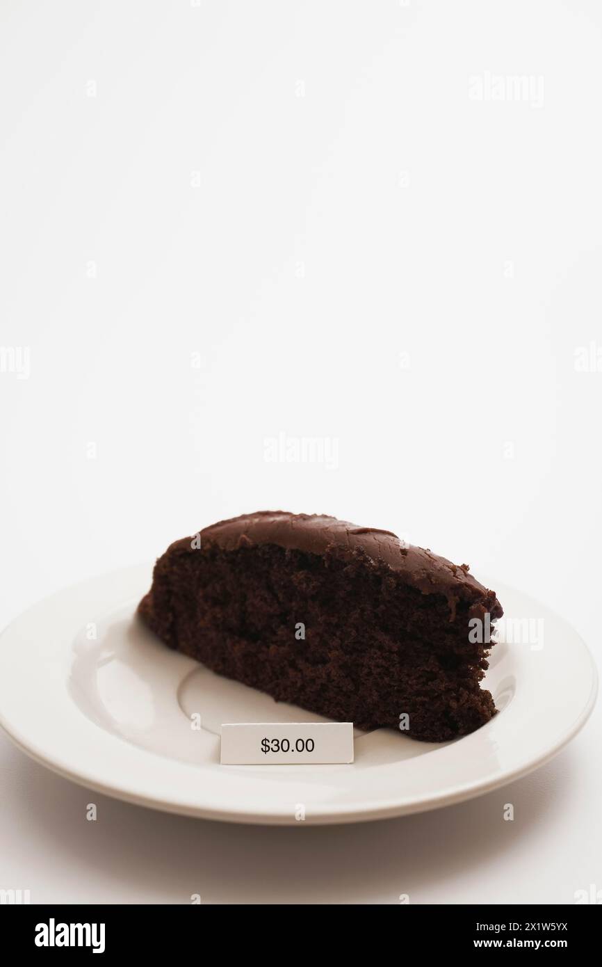 Close-up of slice of chocolate cake with rich creamy frosting and an expensive price tag of $30.00 dollars on white background, Studio Composition Stock Photo