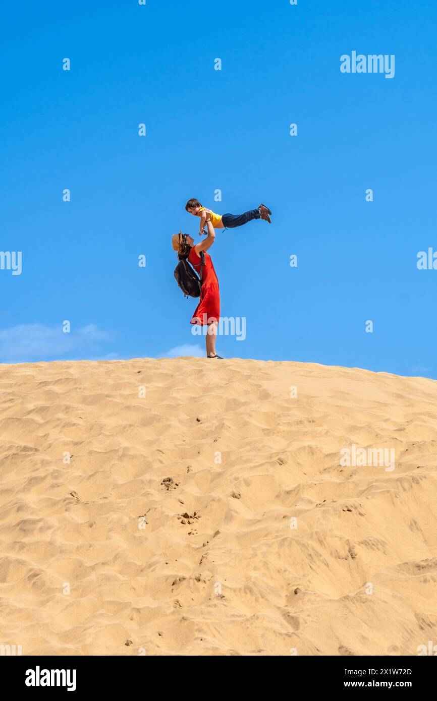 Mother lifting child smiling in the dunes of Maspalomas in summer, Gran Canaria, Canary Islands Stock Photo
