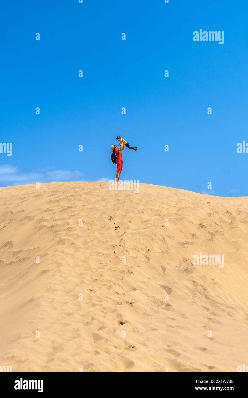 Mother lifting child smiling in the dunes of Maspalomas on vacation, Gran Canaria, Canary Islands Stock Photo