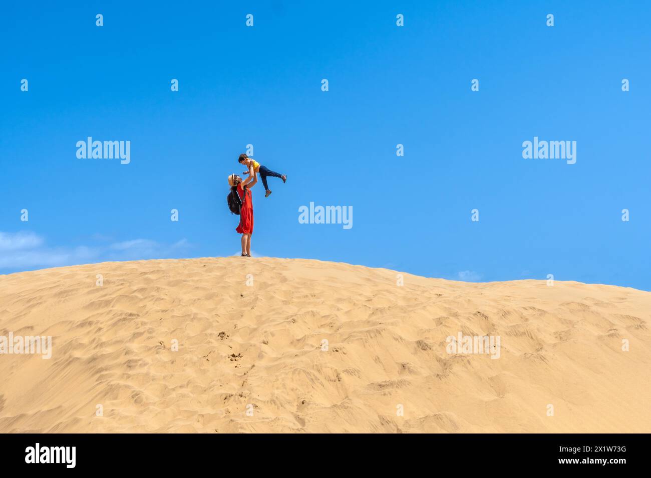 Mother lifting child smiling in the dunes of Maspalomas in summer, Gran Canaria, Canary Islands Stock Photo