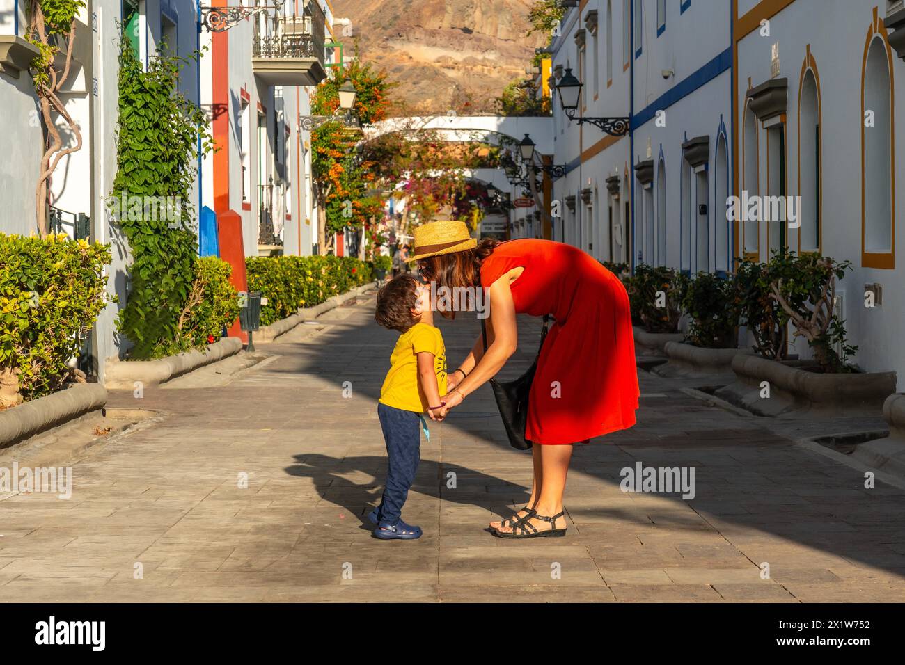 Mother in a red dress and her son walking in the port of the town Mogan in Gran Canaria. Family vacation Stock Photo