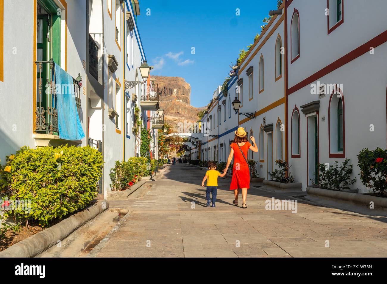 Mother in a red dress and her son walking in the port of the town Mogan in Gran Canaria. Family vacation Stock Photo