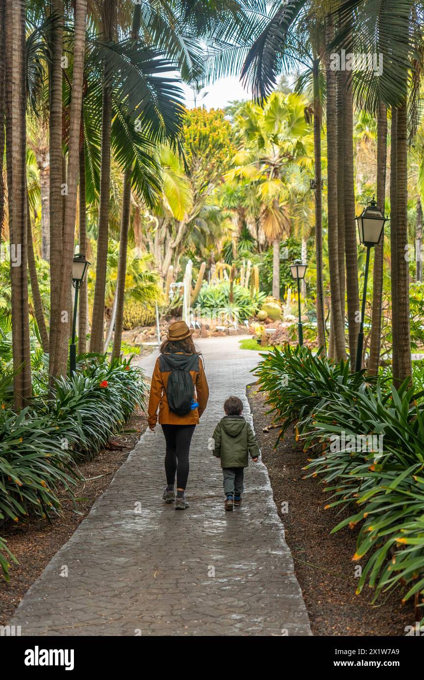 A mother with her son walking in a tropical botanical garden with many palm trees, family vacation concept Stock Photo