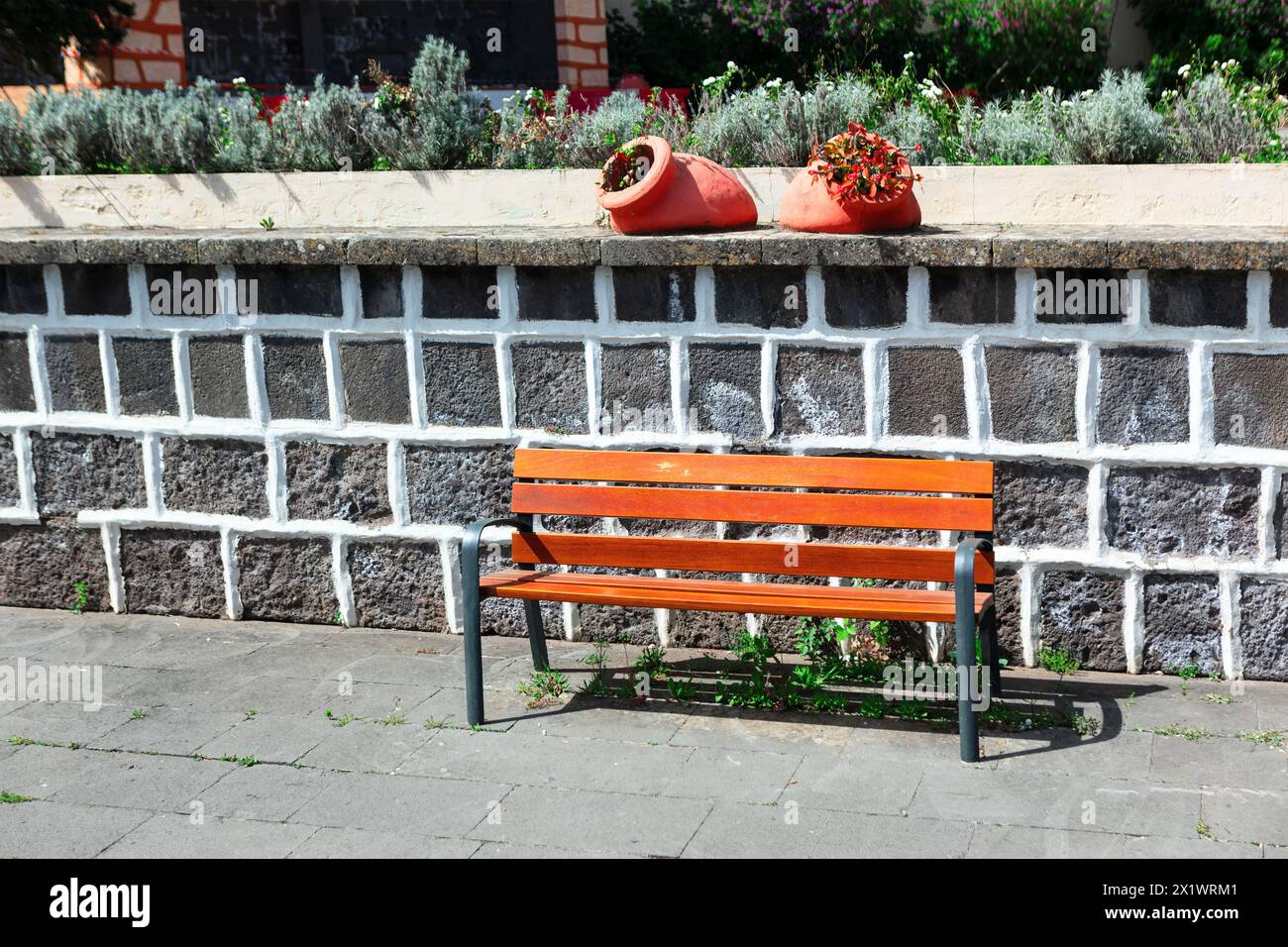 Wooden bench in front of a stone wall with flowers in pots Stock Photo ...