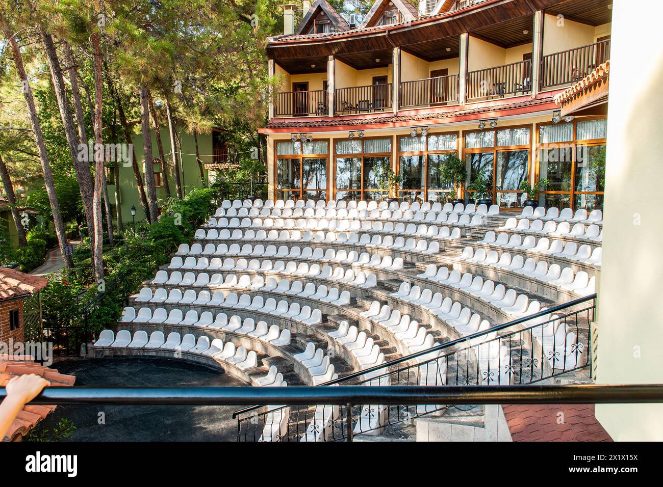 Open-air amphitheater for evening performances at a coastal hotel, surrounded by lush vegetation and tall pine trees Stock Photo