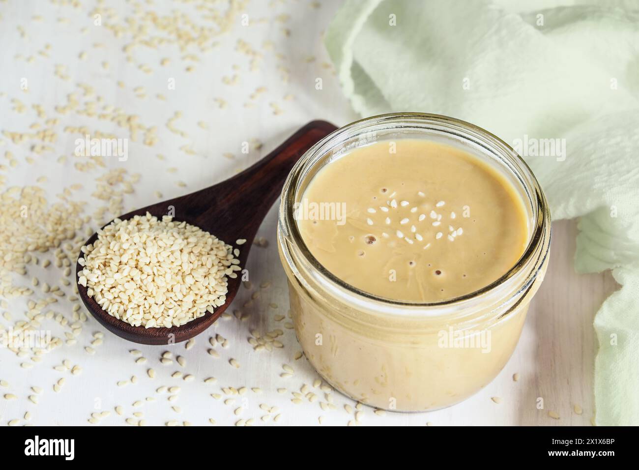 Top view of mason jar filled with tahini. Wooden spoon overflowing with sesame seeds. Top view. Stock Photo