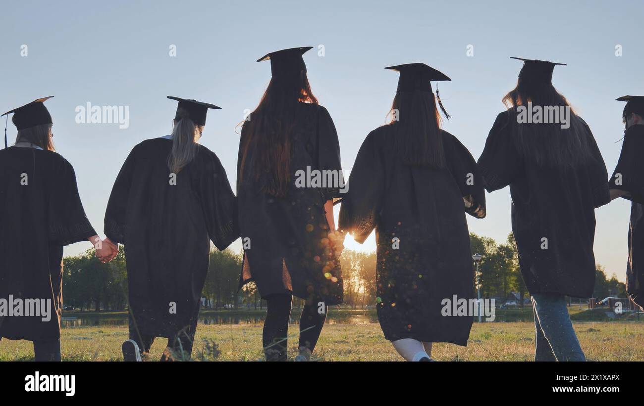 Graduate students walking through an evening meadow at sunset. Stock Photo
