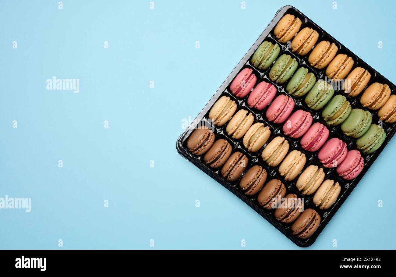 Multi-colored macarons on a blue background in a plastic box, top view. Copy space Stock Photo