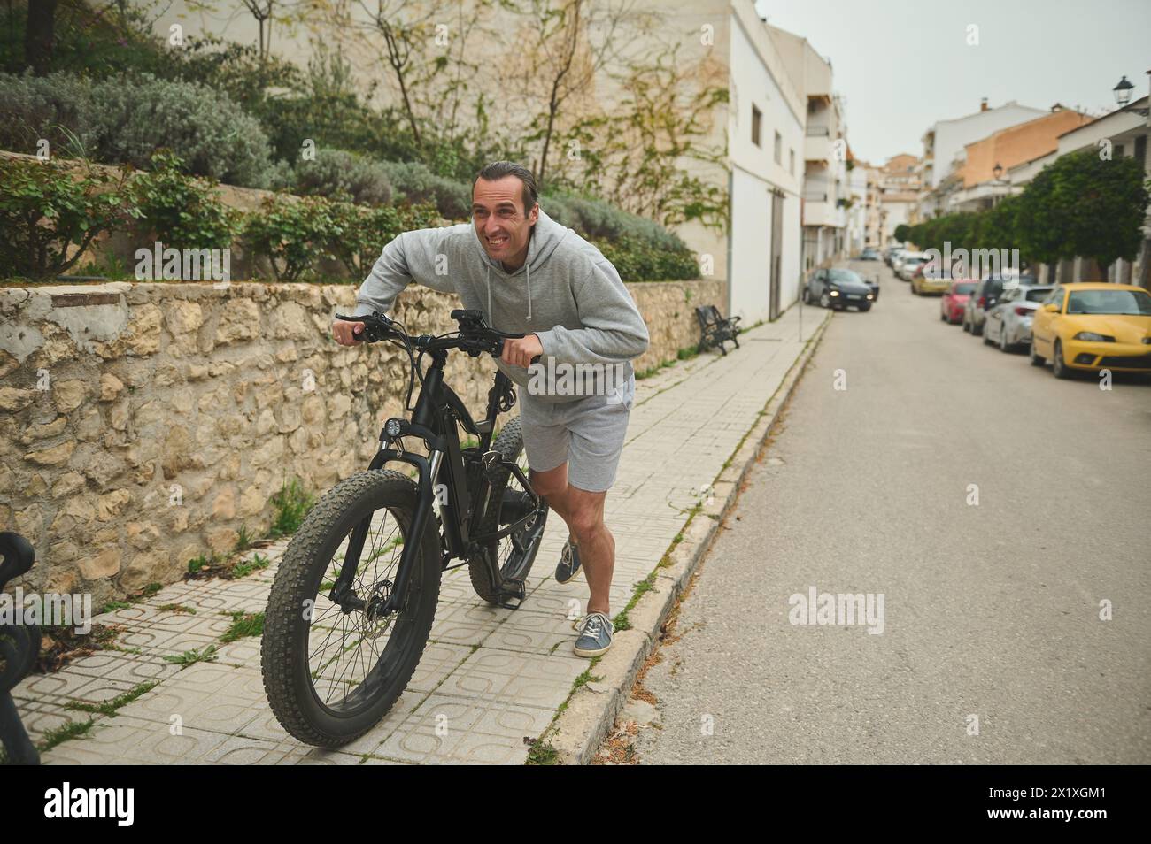 Caucasian young man 40 years old, pushing electric mountain bike up the street. Active lifestyle. Sport. Adventure travel on bicycle. Using el-bicycle Stock Photo